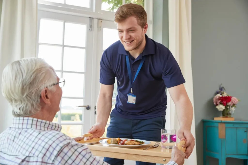 Carer assisting elderly man with meal delivery and nutrition at home in Sussex and Surrey