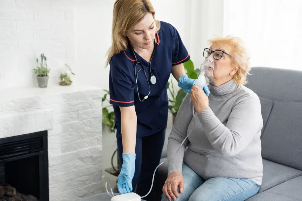 Nurse assisting elderly woman with nebuliser treatment at home in Sussex and Surrey