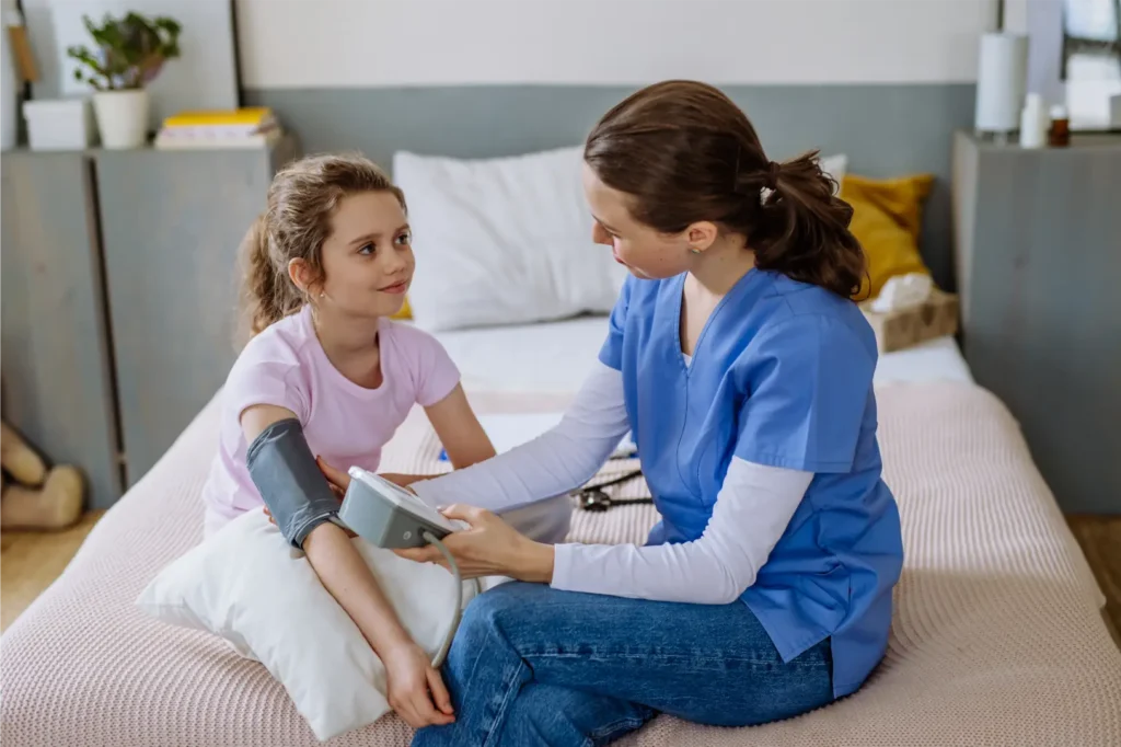 Healthcare professional checking a child’s blood pressure in a calm home setting